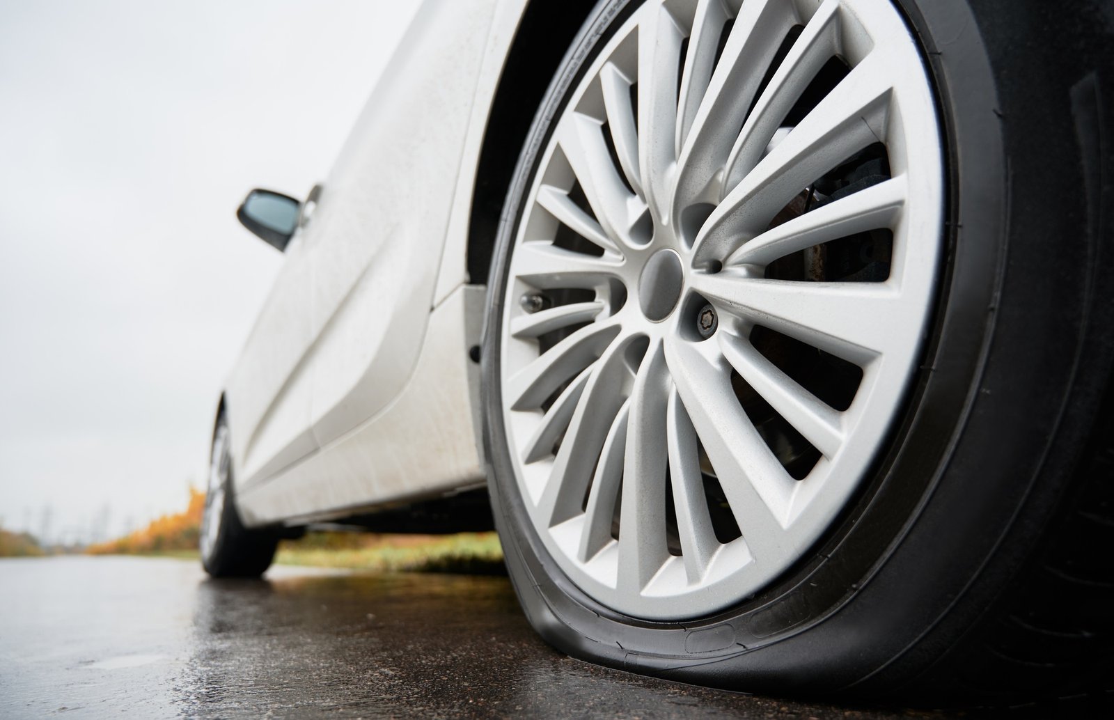 Stopped white car with punctured car tire on a roadside